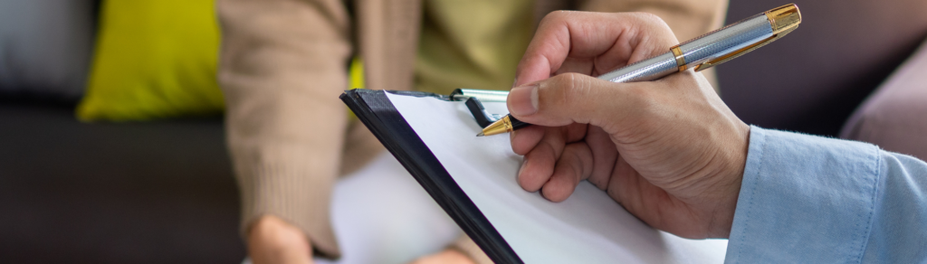 Hand holding a pen writing on a piece of paper clipped on clipboard