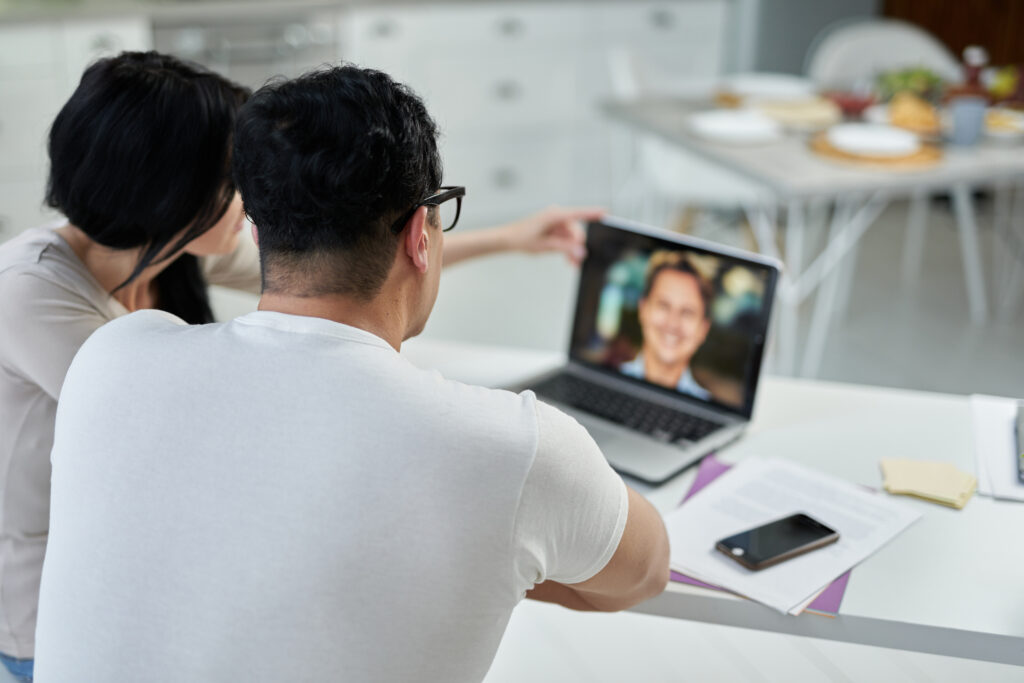 Rear view of middle aged hispanic couple, man and woman communicating with tutor during online training course while studying remotely, using laptop at home. Distant education for adults